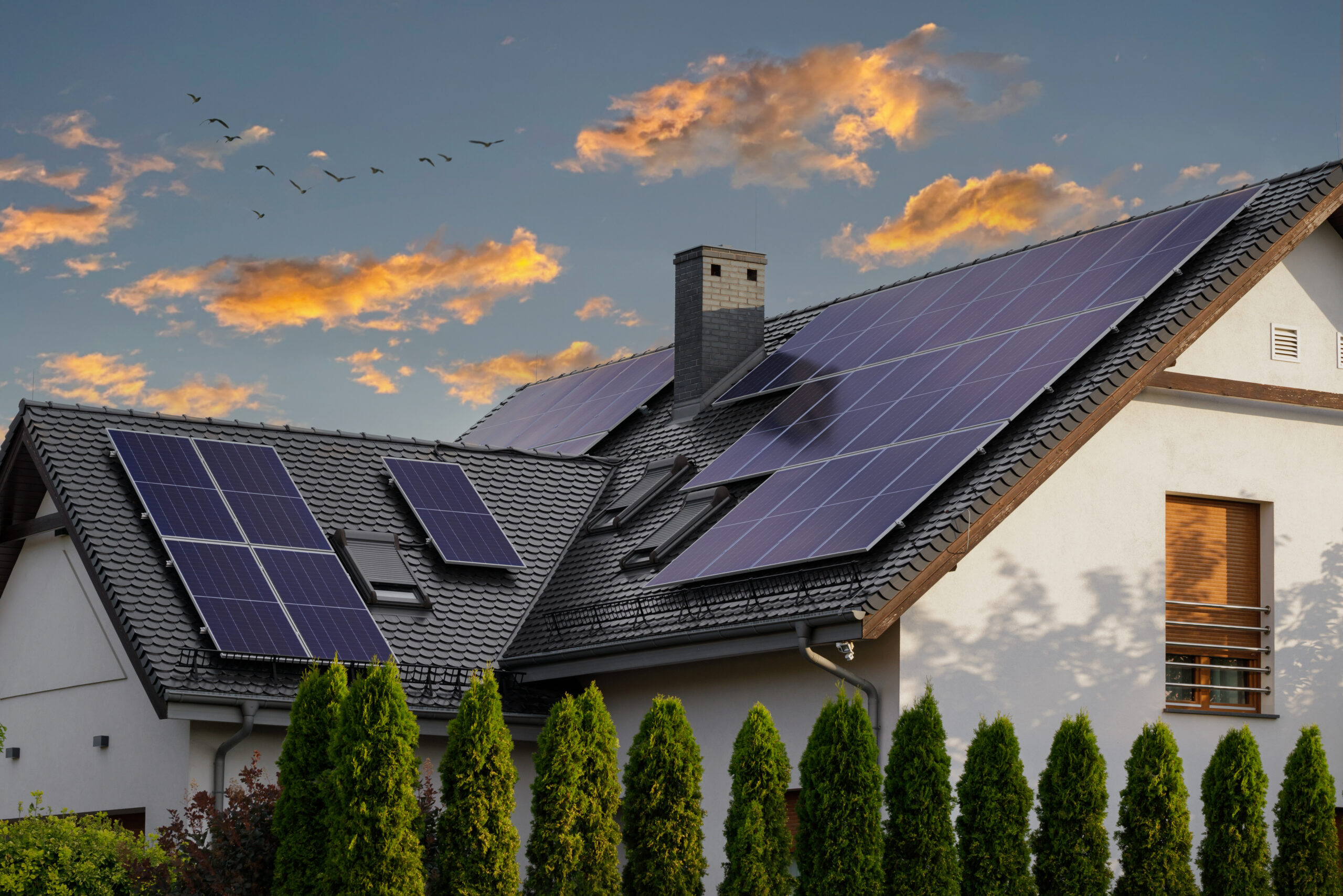 Large modern house with solar panels on a pitched roof. Natural light at sunset. Blue solar panels.